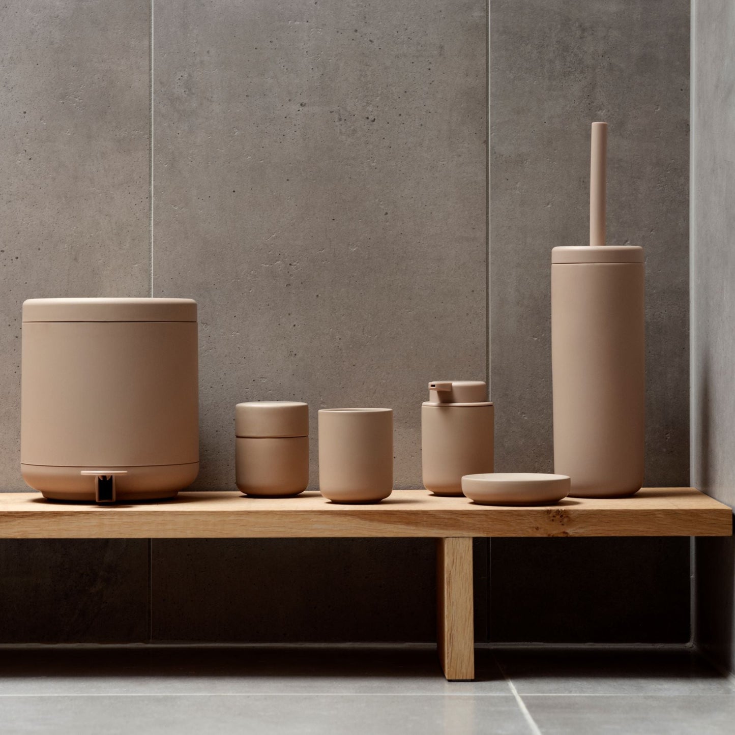 Set of beige ceramic bathroom accessories on a wooden shelf against a gray tiled wall.